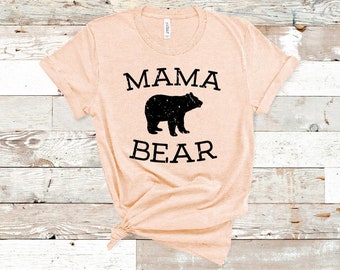 May include: A peach-colored t-shirt with the text "MAMA BEAR" in black lettering. A black silhouette of a bear is centered between the words.