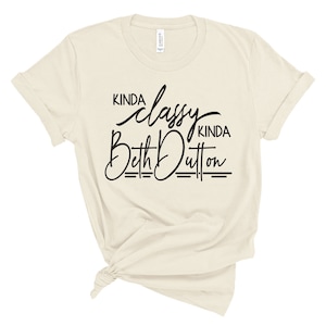May include: A beige t-shirt with black text that reads "Kinda classy Kinda Beth Dutton".