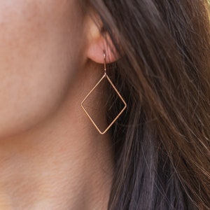 Peut inclure: Une paire de boucles d'oreilles en forme de diamant de couleur or avec un design simple.