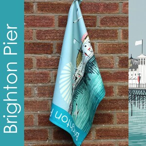 Może przedstawiać: Niebieski i biały ręcznik kuchenny z kolorową ilustracją mola w Brighton. Na ręczniku nadrukowany jest tekst "Brighton Pier".