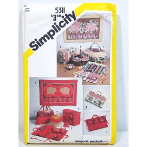 May include: A Simplicity 5311 sewing pattern envelope featuring illustrations of quilted craft projects including bags, baskets, and wall hangings with rabbit and pig motifs in red, cream, and floral patterns. The text includes Simplicity 5311.