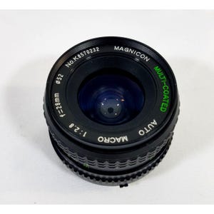May include: A black Magnicon camera lens with the text "MULTI-COATED" in green. The lens has a 52mm diameter and a focal length of 28mm. The lens also has the text "AUTO MACRO" and "1:2.8".