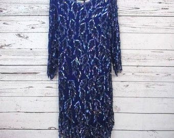 Peut inclure: Une robe bleue à paillettes avec un motif de feuilles. La robe a un col rond et des manches trois quarts.