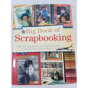 May include: A hardcover book titled "Big Book of Scrapbooking" with a red spine. The cover features photos, including children, and the text "Ideas & inspiration from embellishments to organizing your workspace!" Scissors are also shown.