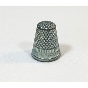 May include: A silver metal thimble with a textured pattern. The thimble is a sewing accessory.