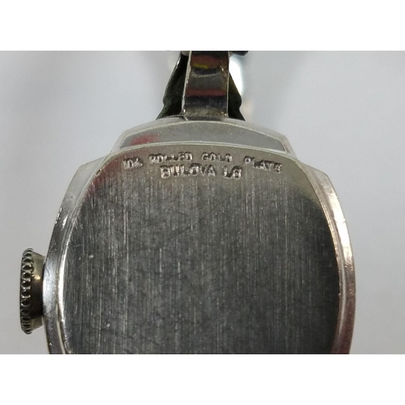 May include: A silver-toned wristwatch with a round face and a silver band. The back of the watch has the text "10k Rolled Gold Plate Bulova 16" engraved on it.