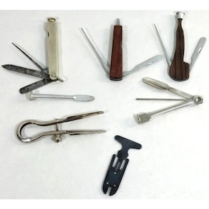 May include: A collection of seven metal and wood multi-tools and pipe cleaning implements. The set includes folding pocket tools with various blades, a silver-toned metal caliper, a T-shaped black plastic tool, and a separate metal tamper.