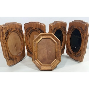 May include: A folding wooden picture frame set featuring four connected oval frames with dark wood grain and decorative carved corners, accompanied by a single, separate octagonal wooden frame positioned in the front center.