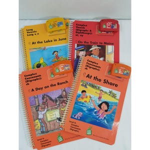 Puede incluir: Una colección de libros educativos para niños con cubiertas coloridas. Los títulos incluyen "At the Lake in June", "On the Train to Maine", "A Day on the Ranch" y "At the Shore". Cada libro tiene una encuadernación en espiral y un dispositivo de lectura naranja o rojo a juego.