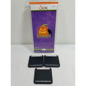 Op de afbeelding: Een set van drie Sizzix-mallen voor knutselen. De mallen zijn zwart en hebben de tekst "For Use in Roller Machines Only". De verpakking toont een paarse achtergrond met een jack-o-lantern en een zwarte vogel, en de tekst "Beware".