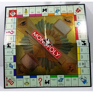 May include: Monopoly board game with a gold and black design. The board features property spaces, Chance and Community Chest cards, and the Monopoly logo. The game board is rectangular and has a classic layout.