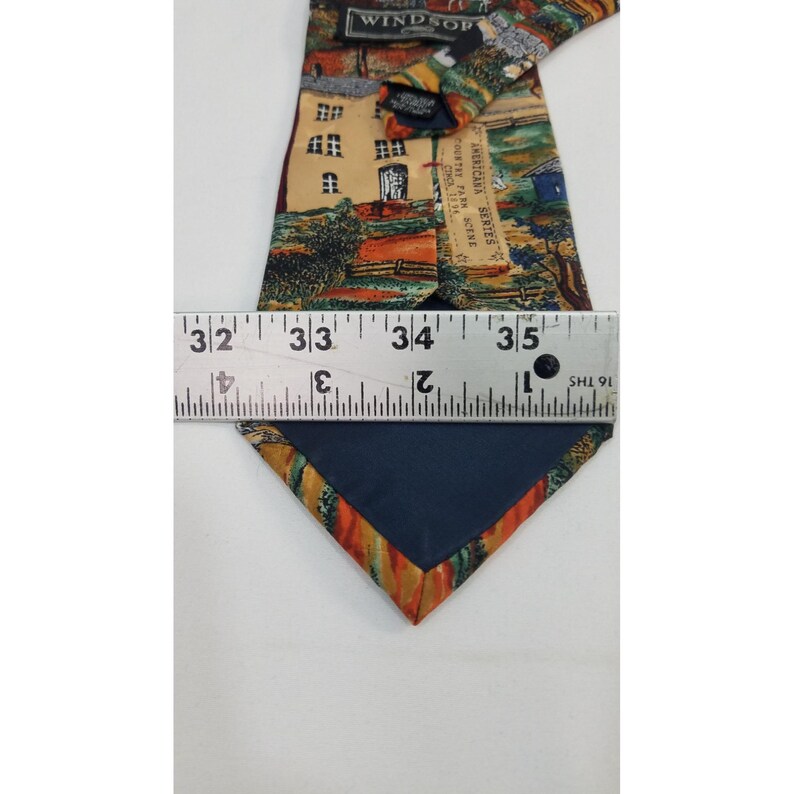 May include: A Windsor Americana Series tie with a scenic landscape design. The tie features a navy blue backing and measures approximately 3.5 inches wide. The design includes a building, trees, and a fence.