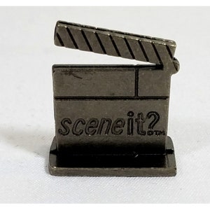 May include: A silver metal game piece shaped like a clapperboard with the words "scene it?" printed on the front.