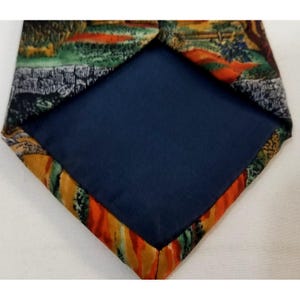 May include: A necktie with a landscape design on the front and a solid navy blue backing. The landscape features green, orange, and brown hues. The tie's edges have a colorful, abstract pattern.