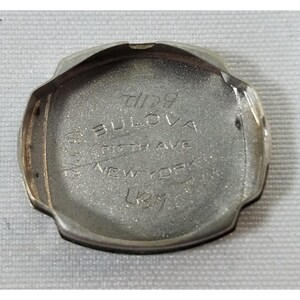 May include: Silver watch case back with the inscription "Bulova Fifth Ave New York 1237".