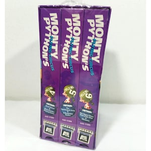 May include: A boxed set of Monty Python's Flying Circus VHS tapes. The purple box features the show's logo and the volume numbers 4, 5, and 6. Each tape's cover includes a cartoon image and episode titles.