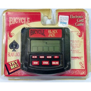 May include: A black handheld electronic Blackjack card game by Bicycle in its original clear plastic blister packaging. The device features a digital screen and red buttons labeled ON/OFF, SOUND, MAX SCORE, BET, VIEW, STICK, and DEAL/HIT.
