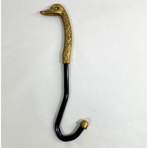 May include: A wall hook featuring a brass duck head handle with detailed feather textures. The neck transitions into a smooth, black, curved metal rod that forms the hook, ending in a small, rounded brass tip at the bottom of the J-shaped design.