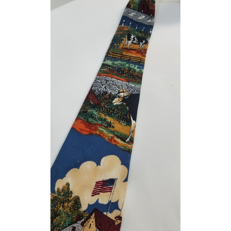 May include: A colorful necktie featuring a rural landscape design. The tie showcases scenes of cows, barns, and an American flag waving in the wind. The tie has a blue background with a variety of colors.