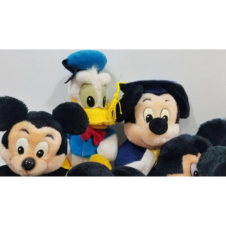 May include: A collection of plush Disney characters, including Mickey Mouse, Donald Duck, and Mickey Mouse in a graduation cap. The plush toys feature vibrant colors and detailed facial features, with Mickey wearing a blue graduation gown.