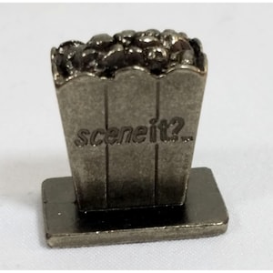May include: A silver metal game piece shaped like a popcorn bucket with the words "Scene It?" on the front.
