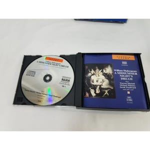 May include: An open CD case containing a silver disc and a booklet. The disc features the text "A Midsummer Night's Dream" and the Naxos logo. The booklet has a blue cover with the play's title and a classical art image.