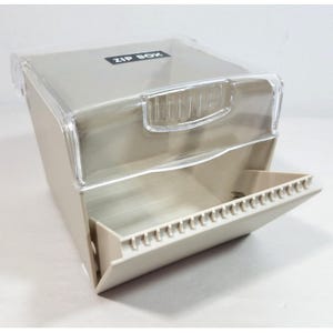 Peut inclure: Un conteneur de rangement en plastique beige étiqueté ZIP BOX avec un couvercle transparent à charnière et un compartiment à ouverture frontale doté d'une rangée de petits séparateurs verticaux le long du bord inférieur pour organiser.