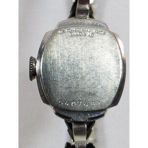 May include: Silver wristwatch with a square face and a silver band. The back of the watch has the text "MK. GOLD-FILL PLATE SWISS MADE" and the number "S407431".