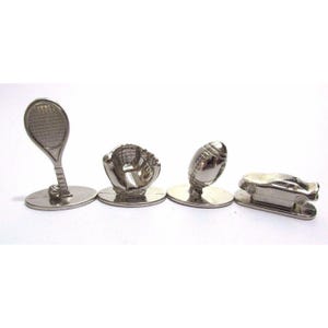 May include: Four silver-toned metal sports-themed objects: a tennis racket, baseball glove, football, and a car. Each object is mounted on a small, round base. The objects are displayed against a white background.