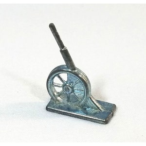 Puede incluir: Una pieza de juego de Monopoly de color plateado con forma de carretilla. La carretilla tiene una sola rueda y un mango que se extiende hacia arriba.