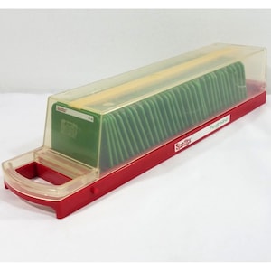 Könnte beinhalten: Eine rote und transparente Sizzix Stanzformen-Aufbewahrungsbox aus Kunststoff. Die Box hat einen transparenten Deckel und enthält grüne Stanzformen. Die Box hat einen Griff und die Wörter "Sizzix" und "Playground" sind auf der Seite aufgedruckt.