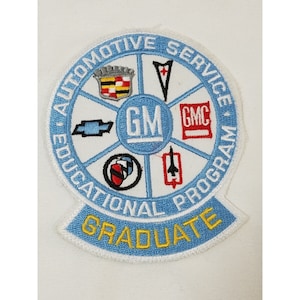 May include: A blue and white embroidered patch with the text "Automotive Service Educational Program Graduate" and the logos of various General Motors brands, including Chevrolet, Cadillac, GMC, and Pontiac.