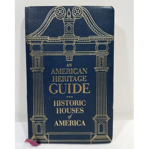 Könnte beinhalten: Ein marineblaues Buch mit dem Titel "An American Heritage Guide" mit goldenen architektonischen Illustrationen. Das Buchcover zeigt auch den Text "Historic Houses of America". Ein rosa Lesezeichenband ist sichtbar.