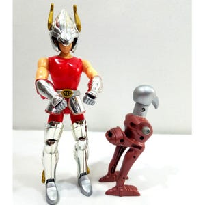 May include: A red and silver action figure of a knight with a silver helmet and armour. The figure is standing next to a red and silver robotic bird. The knight has gold accents on the helmet.