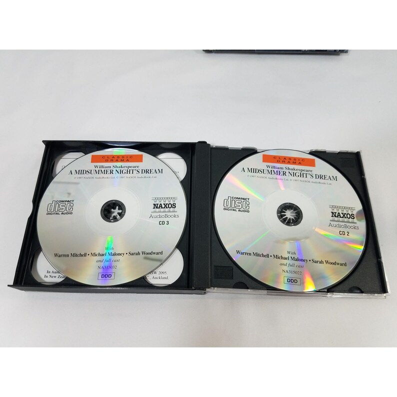 May include: Two open black CD cases with silver discs. The discs are labeled "A Midsummer Night's Dream" by William Shakespeare. The cases are labeled "NAXOS Audiobooks CD 3" and "CD 2".