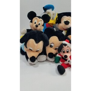 May include: A collection of plush Disney character toys, including Mickey Mouse, Donald Duck, and Pluto. Mickey Mouse is featured in various poses, including one wearing a graduation cap. The toys are soft and colorful, with black, red, and yellow accents.