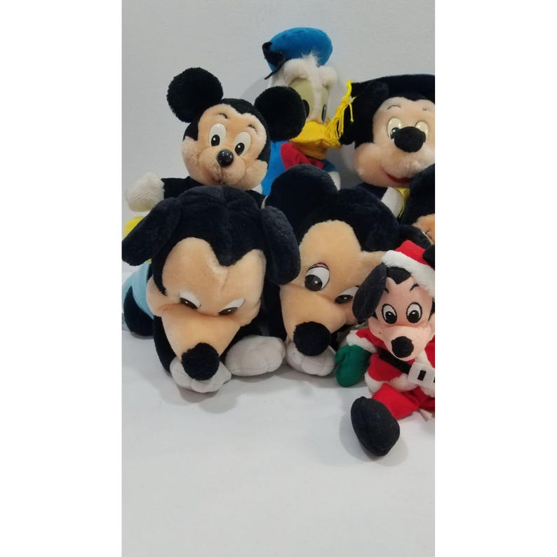 May include: A collection of plush Disney character toys, including Mickey Mouse, Donald Duck, and Pluto. Mickey Mouse is featured in various poses, including one wearing a graduation cap. The toys are soft and colorful, with black, red, and yellow accents.
