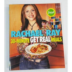 Puede incluir: Portada de libro de cocina con Rachael Ray sosteniendo un plato de comida. El título es "Rachael Ray 30-Minute Get Real Meals" en texto azul y amarillo. El logotipo de Food Network es visible. La portada tiene una paleta de colores cálidos.