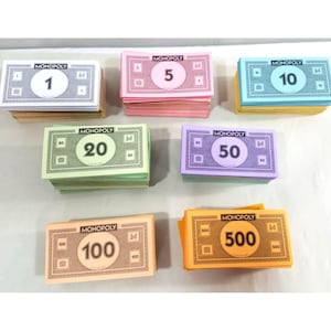 Könnte beinhalten: Verschiedene Stapel Monopoly-Geldscheine in verschiedenen Stückelungen sind zu sehen. Die Geldscheine sind in Farben wie Weiß, Rosa, Blau, Grün, Lila, Pfirsich und Orange gehalten. Das Monopoly-Logo ist aufgedruckt.
