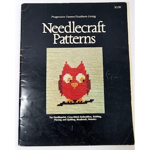 Op de afbeelding: Een boek getiteld "Needlecraft Patterns" met een rood uil-kruissteekontwerp op de omslag. Het boek bevat patronen voor naaldkunst, kruissteekborduren, breien, patchwork en quilten, kralenwerk en mozaïeken.