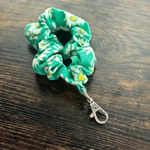 May include: A green scrunchie with a white daisy print and a silver metal key chain clip.