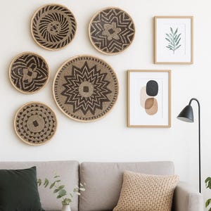 May include: A living room scene featuring woven wall baskets with geometric patterns, framed art, and a light gray sofa with decorative pillows. A round wooden coffee table and a black floor lamp complete the decor. The baskets are in shades of brown and beige.