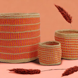 Puede incluir: Tres cestas tejidas con un patrón de rayas rosa y naranja. Las cestas están hechas de materiales naturales y son perfectas para almacenamiento o decoración.