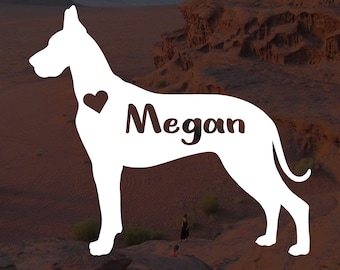 Może przedstawiać: Biała sylwetka dog niemiecki z imieniem "Megan" i sercem na klatce piersiowej. Pies stoi na skalistym, pustynnym krajobrazie.