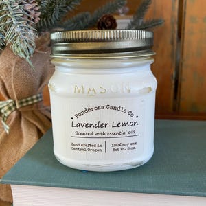 May include: A white Mason jar candle with a gold lid, labeled "Ponderosa Candle Co. Lavender Lemon." The label also states "Scented with essential oils" and "Net Wt. 8 oz.". The candle sits on a stack of books.