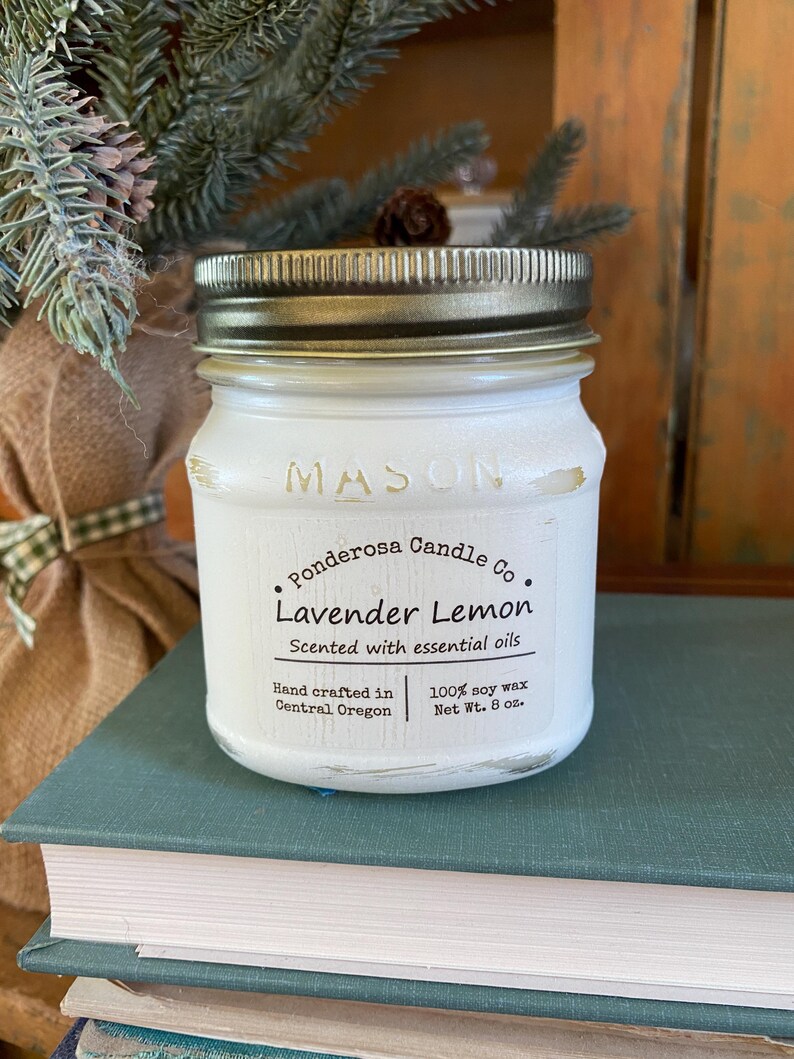 May include: A white Mason jar candle with a gold lid, labeled "Ponderosa Candle Co. Lavender Lemon." The label also states "Scented with essential oils" and "Net Wt. 8 oz.". The candle sits on a stack of books.