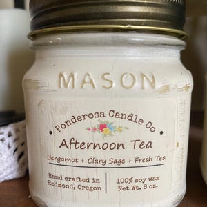 May include: A white painted Mason jar candle with a gold lid. The label reads "Ponderosa Candle Co. Afternoon Tea" with scent details. The candle is hand-crafted in Redmond, Oregon, and contains 8 oz of 100% soy wax.