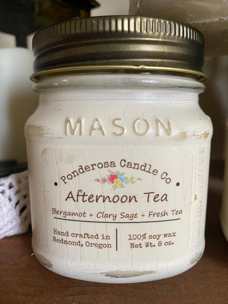 May include: A white painted Mason jar candle with a gold lid. The label reads "Ponderosa Candle Co. Afternoon Tea" with scent details. The candle is hand-crafted in Redmond, Oregon, and contains 8 oz of 100% soy wax.