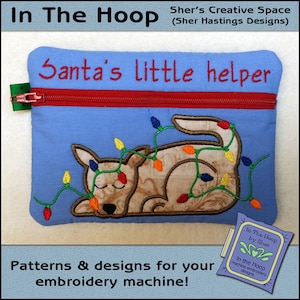 May include: A blue zippered pouch with a brown dog embroidered on it. The dog is wearing a string of colorful lights. The text "Santa's little helper" is embroidered above the dog. The text "In The Hoop by Sher" is on a small tag attached to the pouch.