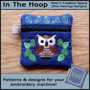 May include: A blue zippered pouch with an embroidered owl design. The owl is brown with white eyes and is surrounded by green leaves. The pouch is labeled "In The Hoop by Sher" and "In the Hoop machine embroidery designs".
